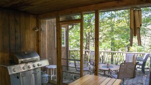 A wooden deck with a grill, outdoor seating, and a view of trees. - Riverfront - main level master bedroom - now with high speed unlimited Internet! (Bowden)