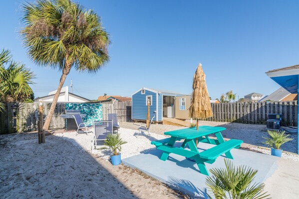A backyard with a blue house, a wooden fence, a picnic table, and a palm tree.