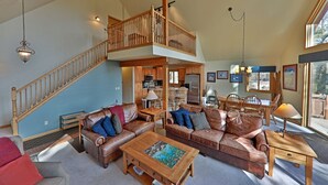 Un vaste espace de vie doté d’un haut plafond, d’un escalier en bois, d’un coin repas avec des meubles en bois et d’une cuisine visible à travers une porte ouverte.