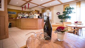 A bar area with a bottle of wine, wine glasses, and a flower vase on a wooden table. - Park Hotel Sacro Cuore (Cavalese)