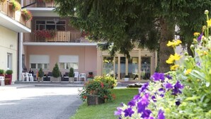 A hotel with a two-story balcony, outdoor seating, and a well-maintained garden with flowers. - Park Hotel Sacro Cuore (Cavalese)