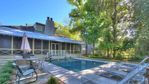 A pool area with lounge chairs, a table with chairs, and a covered patio. - Beautiful Cottage with Private Pool & Large Screened porch in Village Area (St Simons Island)