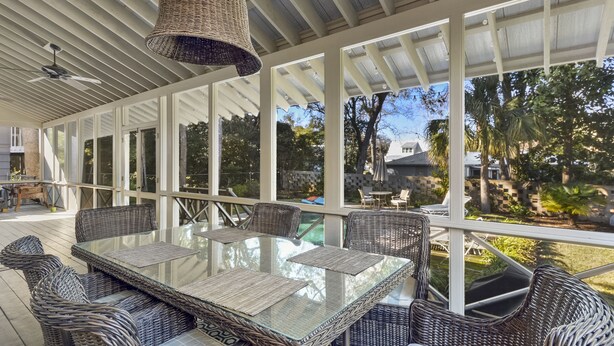 An outdoor patio with a glass table and wicker chairs, surrounded by large windows and a ceiling fan. - Beautiful Cottage with Private Pool & Large Screened porch in Village Area (St Simons Island)