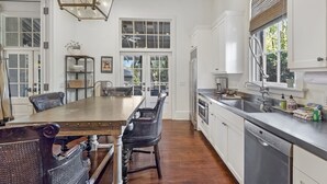 A spacious kitchen with white cabinets, a wooden dining table, and a built-in dishwasher. - Beautiful Cottage with Private Pool & Large Screened porch in Village Area (St Simons Island)