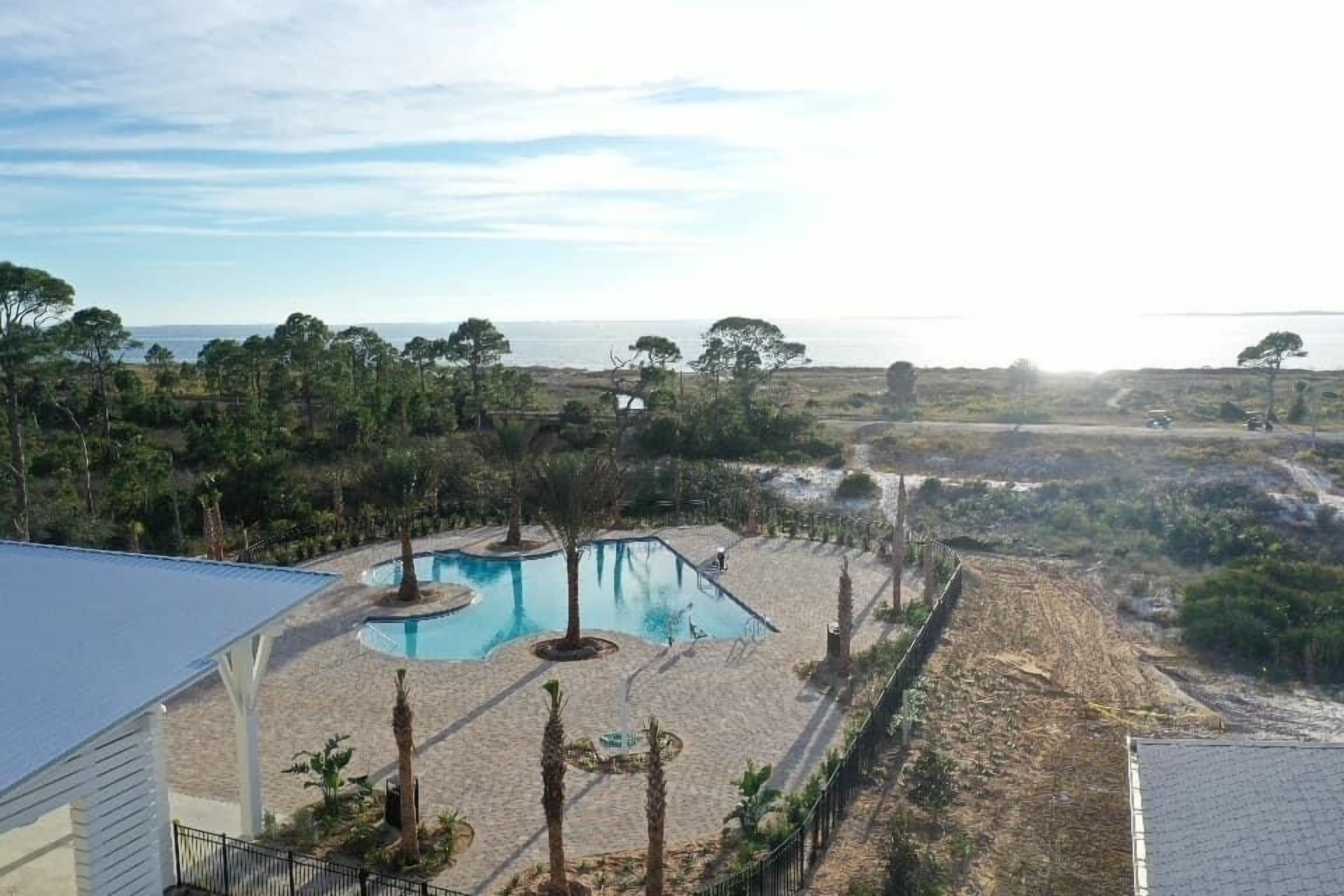 A pool area with a view of the ocean, surrounded by trees and a fenced pathway.