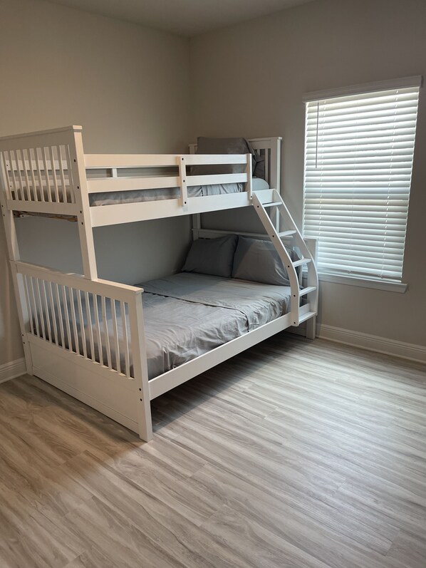 Un lit superposé avec une échelle, une fenêtre avec des stores et un plancher en bois de couleur claire.