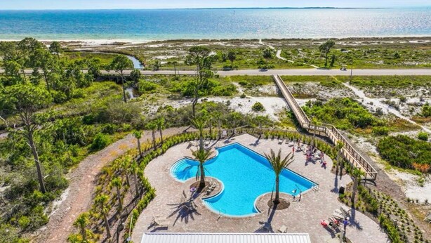 An aerial view of a resort with a central swimming pool, surrounded by pathways and greenery, overlooking a beach and ocean. - The Heron Beach House in Windmark / Mexico Beach, 2 Pools & 5 min walk to Beach. (Port St Joe)