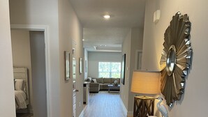 A hallway with a wooden floor, a woven rug, a console table with a lamp, and a decorative mirror. - The Heron Beach House in Windmark / Mexico Beach, 2 Pools & 5 min walk to Beach. (Port St Joe)