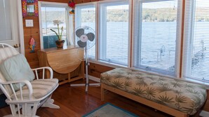 A cozy room with a wooden desk, a rocking chair, a bench with a leaf-patterned cushion, and a standing fan. - Lucky Catch: Best Cottage on the Best Lake! (Penn Yan)