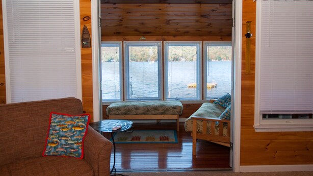 A cozy cabin interior with a wooden floor, a bench, a small table, and a couch. - Lucky Catch: Best Cottage on the Best Lake! (Penn Yan)