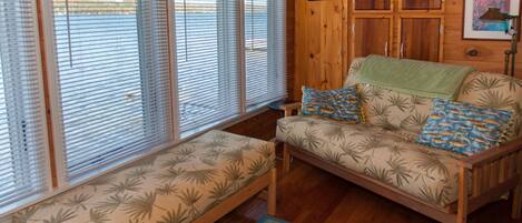 A wooden cabin interior with a sofa and bench, wooden walls, and a view through large windows.