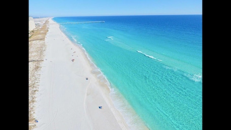 A beach with clear turquoise water, a sandy shore, and a pier extending into the sea.