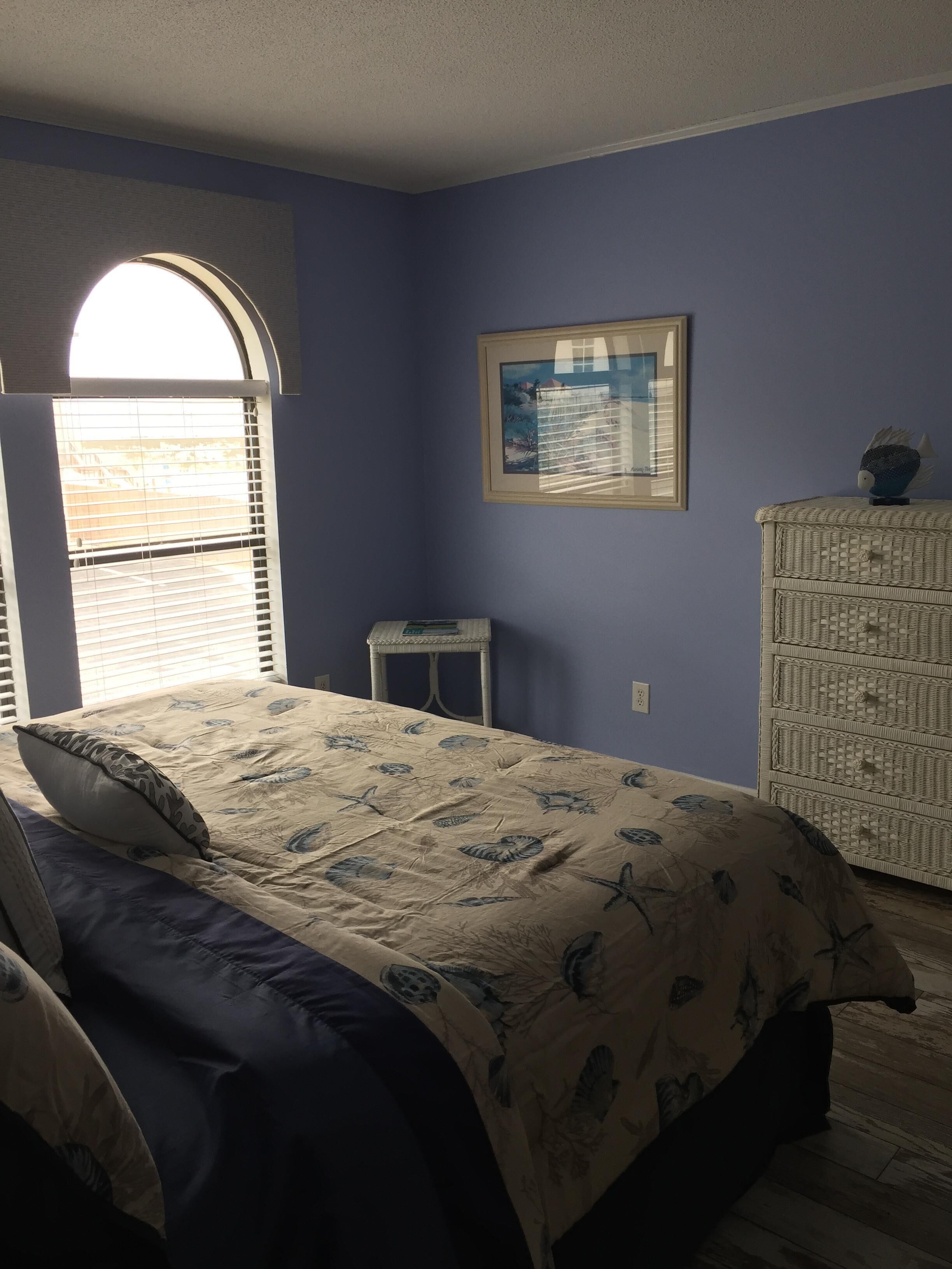 A bedroom with a bed, a small table, a dresser, and a window with blinds.