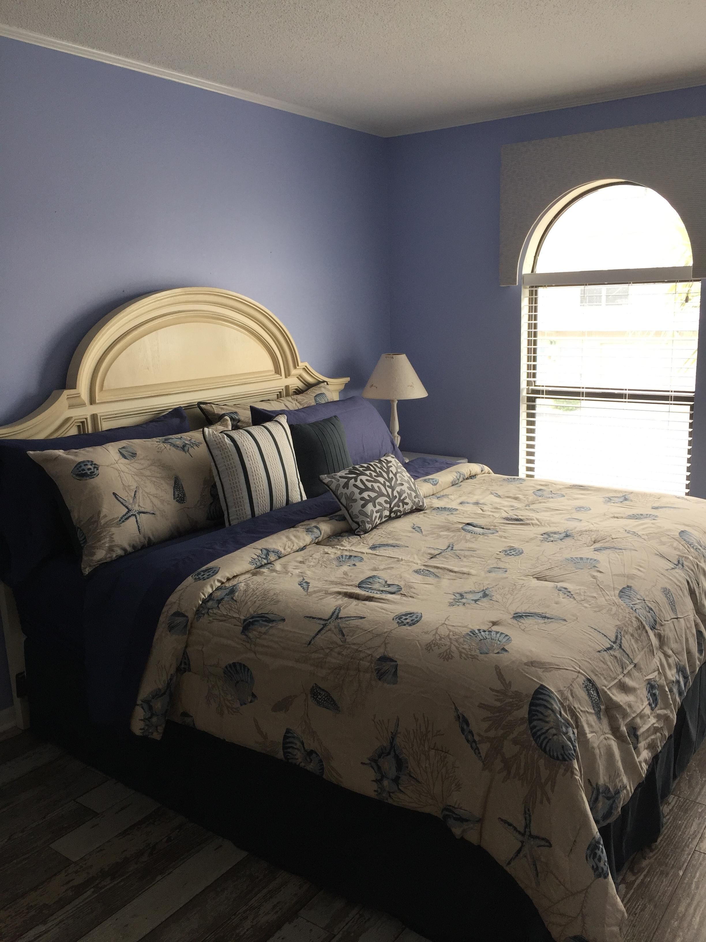 Een slaapkamer met een bed, voorzien van een sprei met bloemen en zeesterrenprint, een houten hoofdbord en meerdere kussens.