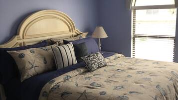 Een slaapkamer met een bed, voorzien van een sprei met bloemen en zeesterrenprint, een houten hoofdbord en meerdere kussens.