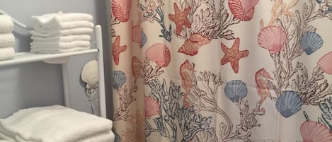 A bathroom with a shower curtain featuring a sea-themed pattern, a towel rack with neatly stacked towels, and a starfish decoration on the wall.
