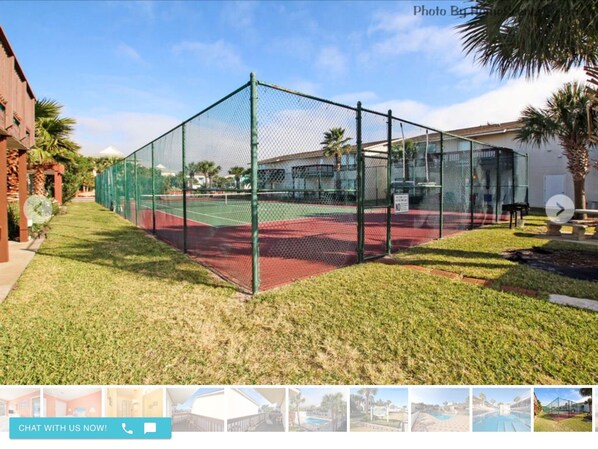 A tennis court enclosed by a green fence, with a building adjacent to it.