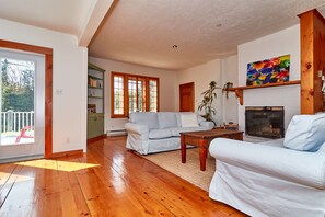 A spacious living room with wooden flooring, a fireplace, and a large window. - Auberge de la Tour et Spa (Orford)