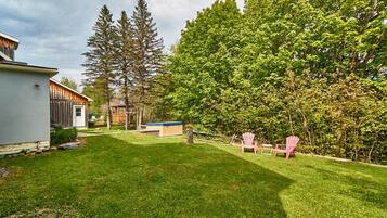 A backyard with a well-maintained lawn, a wooden shed, a hot tub, and two Adirondack chairs.