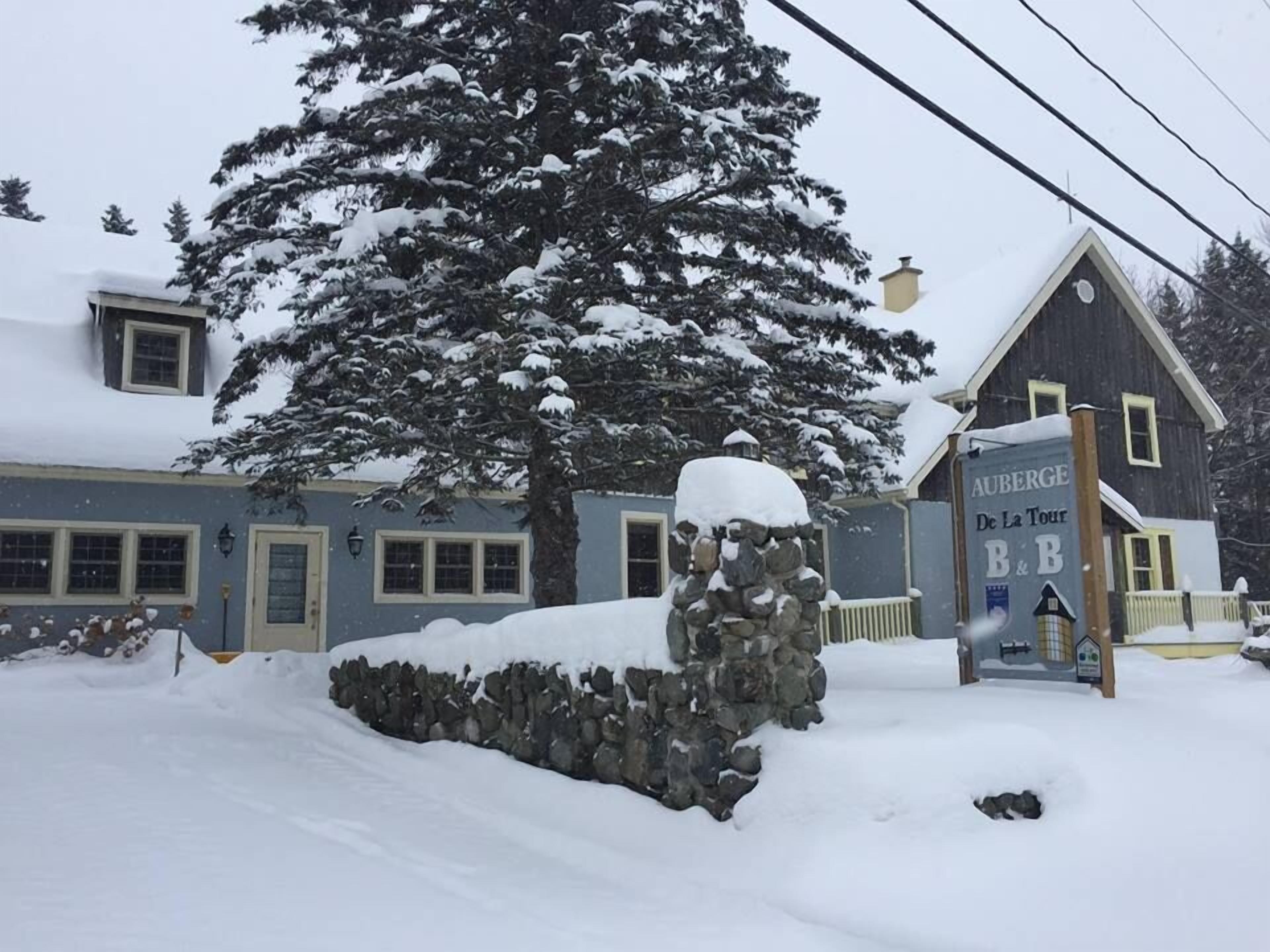 A snow-covered building with a stone wall and a sign reading "AUBERGE De La Tour B&B".