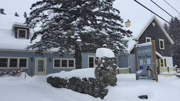 A snow-covered building with a stone wall and a sign reading "AUBERGE De La Tour B&B".