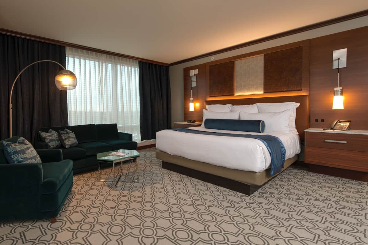Une chambre d’hôtel avec un grand lit, un canapé vert foncé, une petite table basse et un lampadaire.