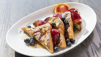 A white plate with French toast, blueberries, strawberries, and a slice of orange on a wooden table.
