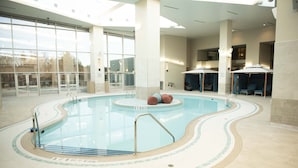 An indoor swimming pool with clear water, tiled floor, and a few lounge chairs. - Resorts World Catskills Casino (Monticello)