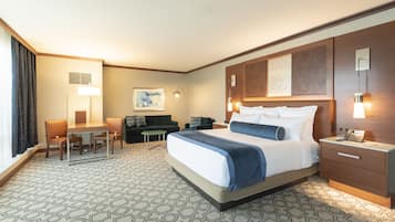 A hotel room with a large bed, a desk with a chair, a sofa, a small table, and a bedside table with a lamp and phone.
