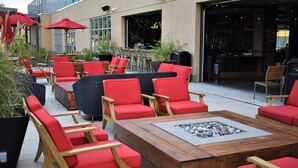 An outdoor seating area with red chairs and tables, a fire pit, and a bar visible through the window. - Resorts World Catskills Casino (Monticello)