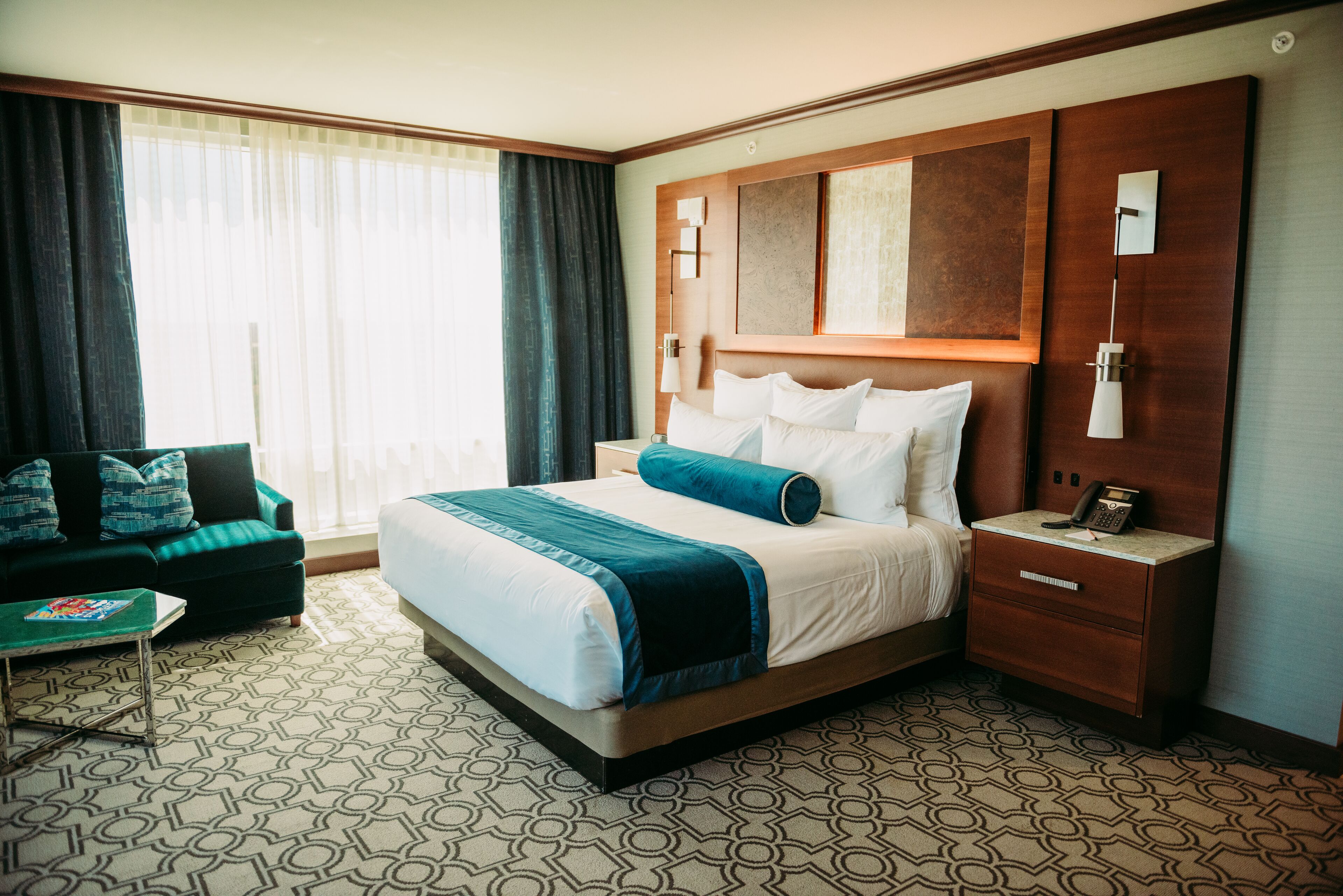 Una camera d'albergo con un letto grande, un comodino, un divano verde e una moquette a fantasia.