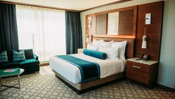 Une chambre d’hôtel avec un grand lit, une table de chevet, une commode, un canapé vert et une moquette à motifs.
