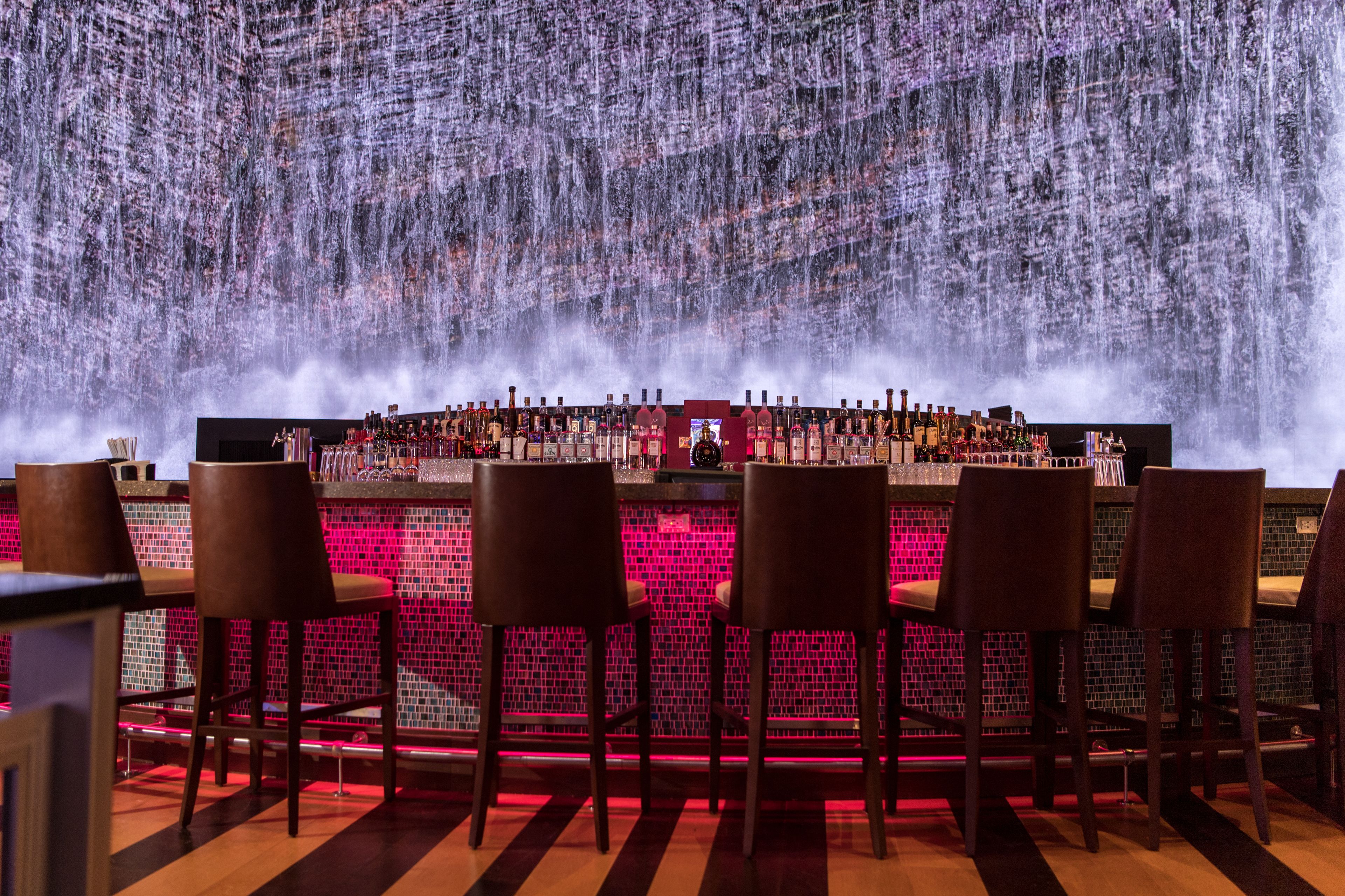 A bar area with a long counter, multiple bottles of alcohol, and bar stools.