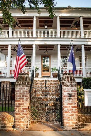 Traditional two-story building with a balcony and entrance marked by a wooden door and brick pillars.