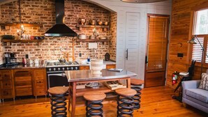 A rustic kitchen with a brick wall, wooden cabinets, a stainless steel island, and a hanging light fixture. - 2BR Historic Suite Perfect Location Downtown Charleston (Charleston)