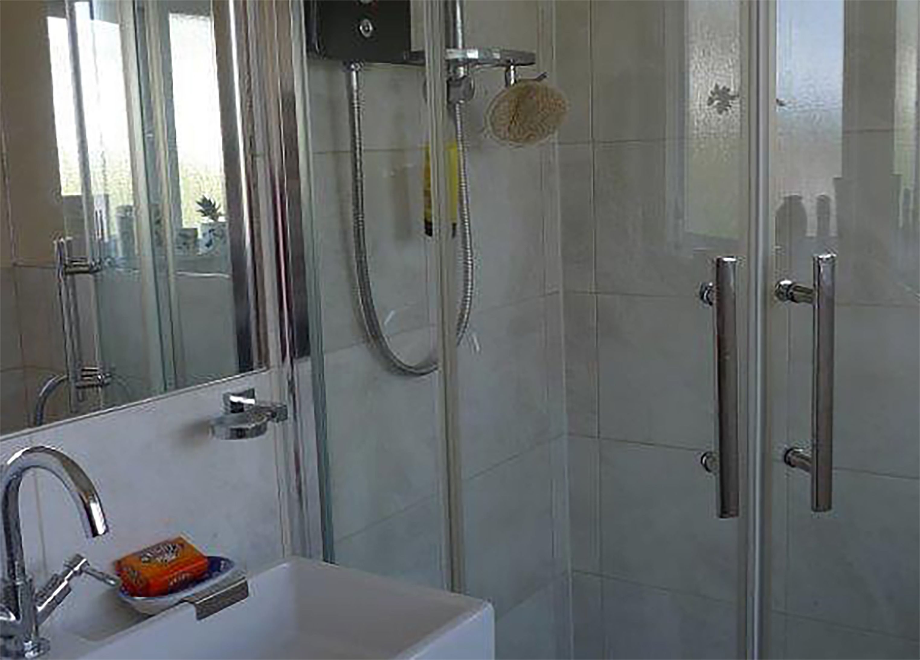 A modern bathroom with a glass shower enclosure, a white sink with a soap dish, and a mirror above the sink.