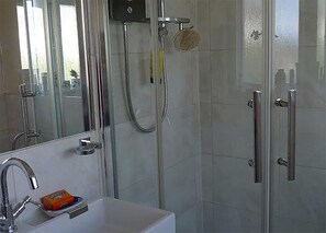 Ein modernes Badezimmer mit einer Duschkabine aus Glas, einem weißen Waschbecken mit Seifenschale und einem Spiegel über dem Waschbecken.