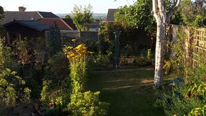 A garden with a red table and chairs, a hot air balloon in the background, and a variety of plants and trees. - A. B&B - Glastonbury (Glastonbury)