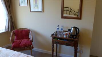 Una habitación de hotel con una cama, una silla, una mesita con botellas de agua, una cafetera y cuadros en la pared.