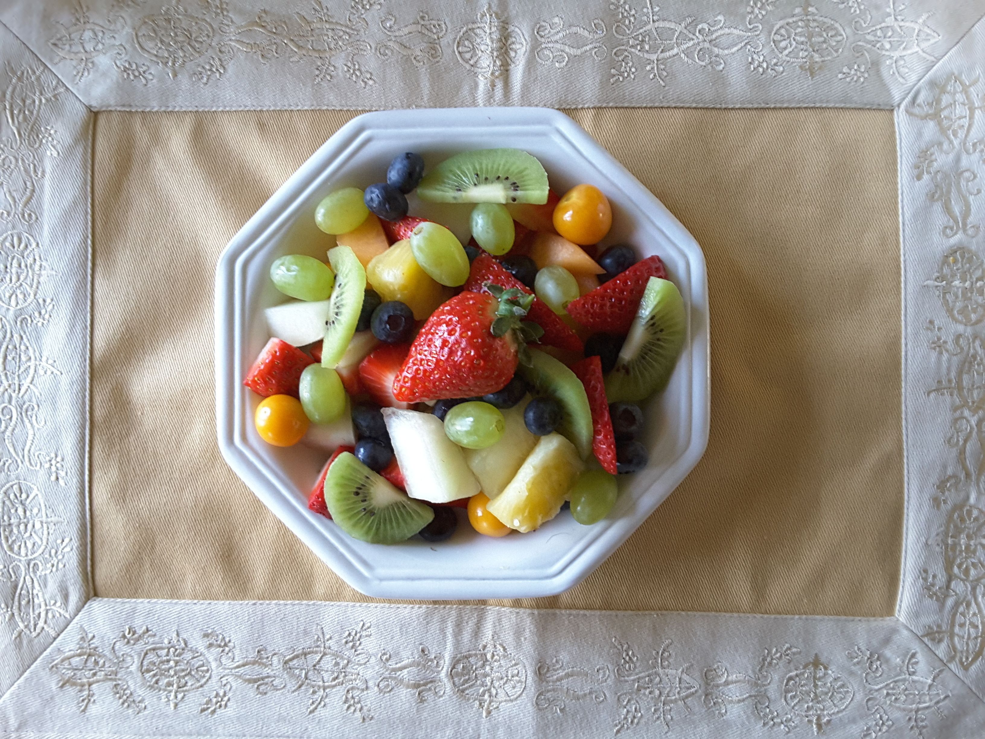 Een witte fruitschaal op een tafel met een tafelkleed met patroon.