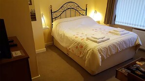 A neatly made bed with a floral bedspread and two pillows, a bedside lamp, and a small table with a remote control. - A. B&B - Glastonbury (Glastonbury)