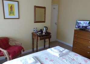 Ein Hotelzimmer mit einem Bett, einer Holzkommode, einem kleinen Tisch mit Toilettenartikeln, einem roten Sessel, einem Spiegel und einem Fernseher.
