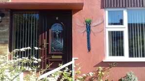 A house with a dark brown door, a window with vertical blinds, and a dragonfly decoration on the wall. - A. B&B - Glastonbury (Glastonbury)