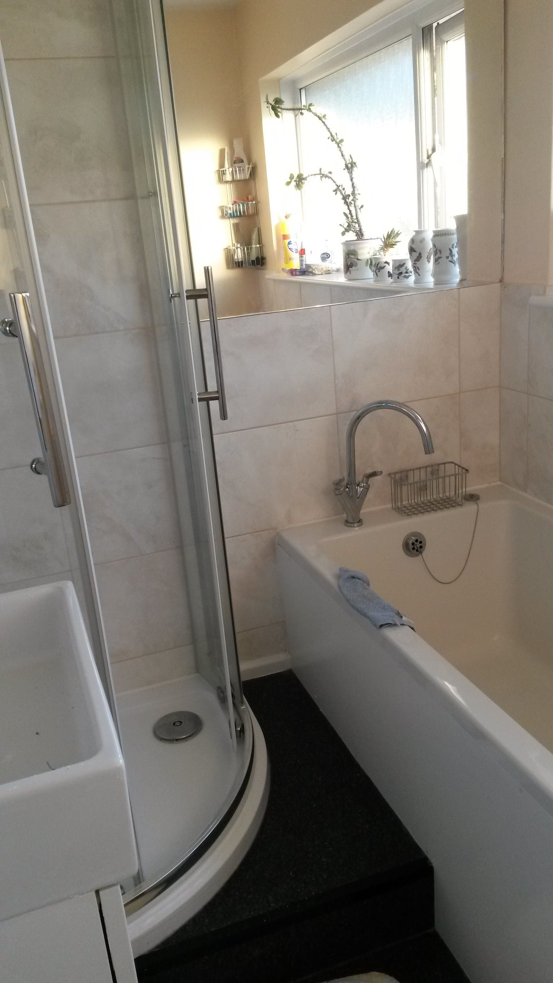 A bathroom with a glass-enclosed shower, a white bathtub, and a window above the sink.