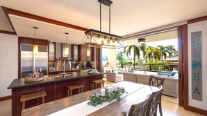 A modern kitchen with a wooden island, bar stools, and a dining area with a table set for four. - Luxurious Beach Villa 3BR/2.5B in KoOlina~FREE WIFI, GYM w/ ALL NEW UPGRADES (Kapolei)