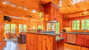 A wooden cabin interior with a central island, wooden cabinets, and large windows. - Luxury Cabin, Casino, Ski, Snow Tube, Golf, Hike, Fish, Hot Tub, Fire Pit, Train (Whittier)