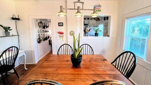 Un coin repas avec une table en bois, quatre chaises, une plante en pot et des luminaires suspendus.