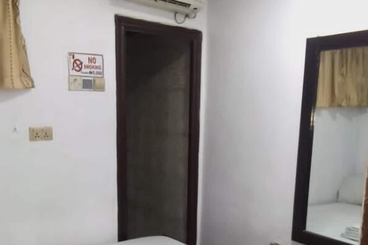 Uma cama de solteiro num quarto com porta, ar condicionado e um espelho na parede.