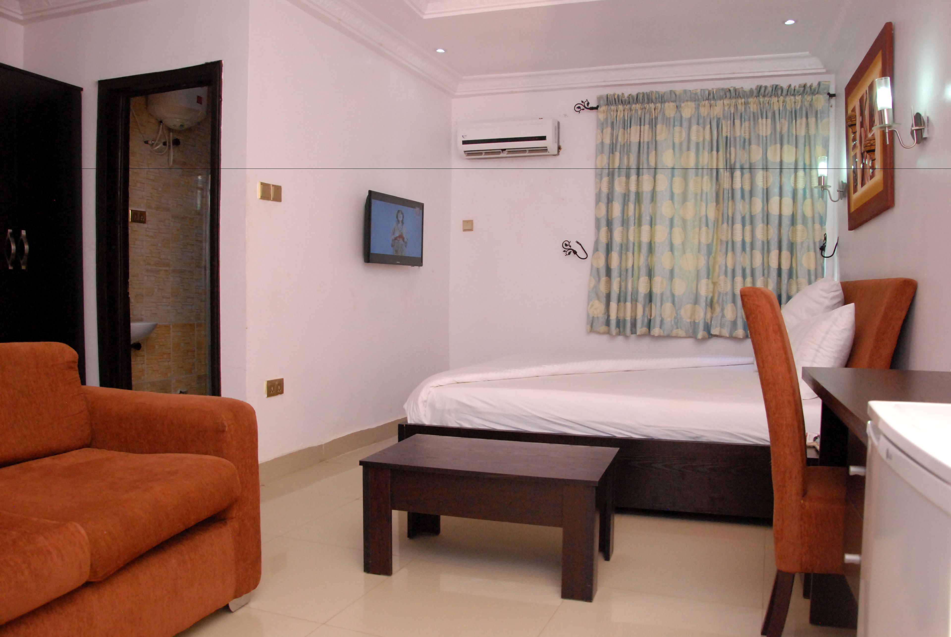 Habitación de hotel con cama, escritorio, silla, aire acondicionado, un cuadro en la pared y ventana con cortinas.