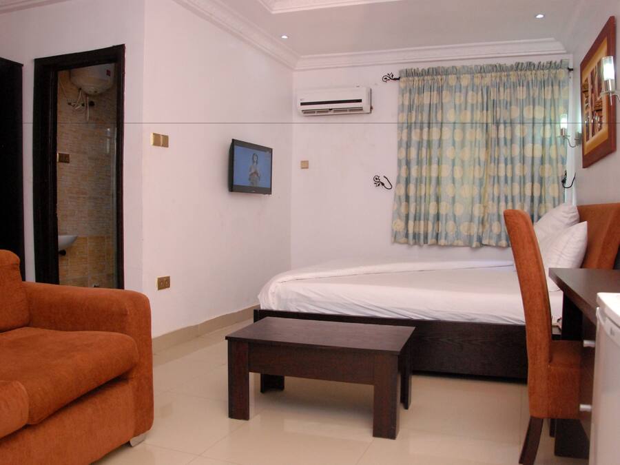 Habitación de hotel con cama, escritorio, silla, aire acondicionado, un cuadro en la pared y ventana con cortinas.